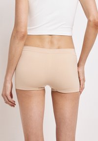 Beige boyshort-underkläder i ett mjukt, stretcht tyg. Har en låg midjeband och en sömlös design för komfort och passform.