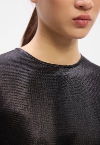 Černý strukturovaný top s kulatým výstřihem, který má jemný lesk a jemný mřížkový vzor. Detailní pohled, zaměřující se na detaily tkaniny.