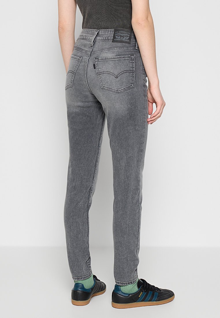 Jeans de tiro alto grises con un diseño ajustado, con bolsillos traseros y una etiqueta de marca en la cinturilla, combinados con zapatillas negras.