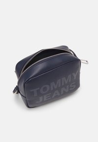 Borsa in ecopelle blu navy con forma rettangolare, zip argentata e grande marchio "TOMMY JEANS" sul davanti. Texture liscia.