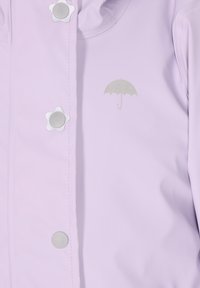 Lila lietussargapmaka ar zvaigžņu formas pogām, sudraba lietussarga logotips uz krūtīm un gluda, ūdensnecaurlaidīga materiāla.