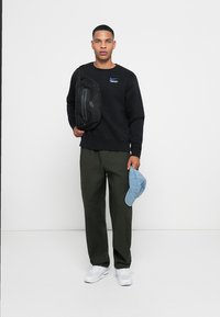 Black sweatshirt with logo, green cargo pants, black crossbody bag, and light blue baseball cap. White sneakers complete the outfit.