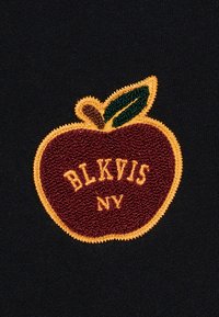 Toppa ricamata con una mela color marrone scuro e una foglia verde, testo giallo "BLKVIS NY", su sfondo di tessuto nero.