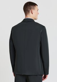 Giacca su misura nera con una texture liscia, uno spacco sul retro e polsini con bottone. Design semplice senza motivi visibili.