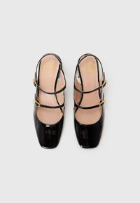 Sorte patentlær slingback-sko med firkantede tær, utsmykket med tre stropper med gullspenner og en myk beige innersåle.