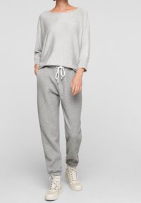 Světle šedý dlouhý rukáv s širokým výstřihem, kombinovaný s texturovanými šedými tepláky s elastickým pasem a šňůrkou. Krémové tenisky.