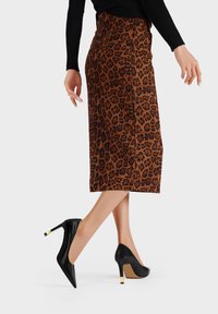 Gonna midi a fantasia leopardata in marrone e nero con una silhouette elegante; abbinata a tacchi alti neri a punta con un accento dorato.