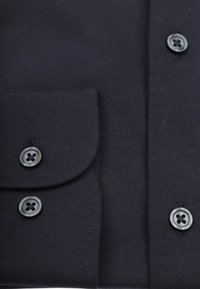 Marineblauwe blouse met een zak, drie zwarte knopen met elk vier gaten, en een gladde, textuurstof.