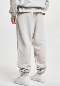 Light grey sweatpants made of soft material, featuring elastic cuffs and a relaxed fit. Paired with white sneakers. Back view.