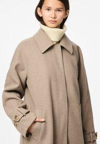 Cappotto di lana beige con ampio colletto, tasche laterali e polsini con bottoni. Texture morbida, taglio dritto, design semplice, adatto per l'abbigliamento casual.