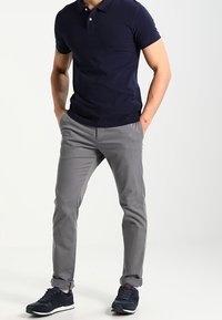 Polo-shirt bleu marine, à manches courtes, avec deux boutons, associé à un pantalon chino gris clair, coupe droite, avec des manchettes retroussées, et des chaussures de sport bleu marine.