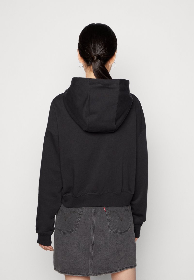 Sudadera negra con capucha y un corte relajado, fabricada en un tejido texturizado y con puños de canalé, combinada con una falda de mezclilla gris oscuro que cuenta con bolsillos traseros.