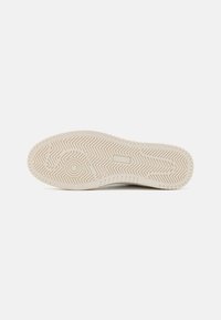 Sole of a sneaker featuring a textured, herringbone pattern in light beige, with a rounded heel and smooth edges.