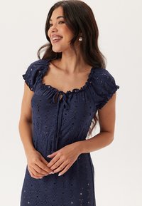 Mörkblå broderad klänning med korta volangärmar, blommönster, detalj med knytning framtill och en figursydd midja som övergår i en utsvängd kjol.