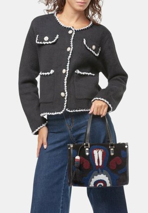 Cardigan in lana nera con bordi bianchi, collo rotondo e bottoni dorati; abbinato a una borsa ricamata nera con motivi colorati e frange.