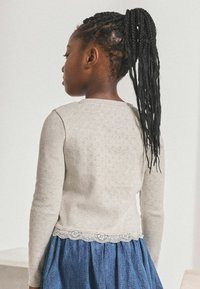 Ljust grått texturerat tröja med långa ärmar och spetskant, kombinerad med en denimkjol, visad bakifrån.