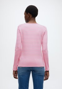 Μακρυμάνικο πουκάμισο σε ροζ με λευκές οριζόντιες ρίγες, με στρογγυλή λαιμόκοψη και απαλή, ομαλή υφή. Φορεμένο με μπλε τζιν παντελόνι.