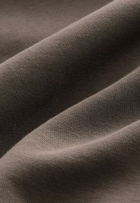 Tessuto di cotone in un color marrone tenue, con una texture liscia caratterizzata da un motivo a maglia fine e un morbido cadere.