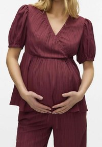 Haut de maternité bordeaux, avec un col en V, des manches courtes bouffantes et un tissu texturé à rayures verticales. Assorti à un pantalon coordonné.