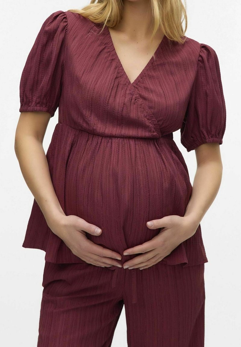 Haut de maternité bordeaux, avec un col en V, des manches courtes bouffantes et un tissu texturé à rayures verticales. Assorti à un pantalon coordonné.