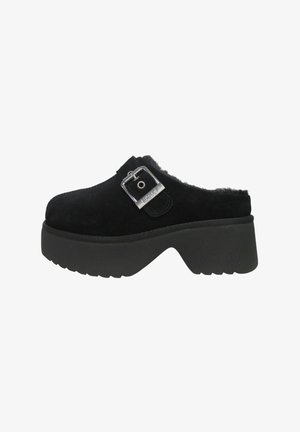 Zoccoli in camoscio nero con fibbia, caratterizzati da una suola spessa nera e un bordo soffice lungo l'apertura per aggiungere texture.