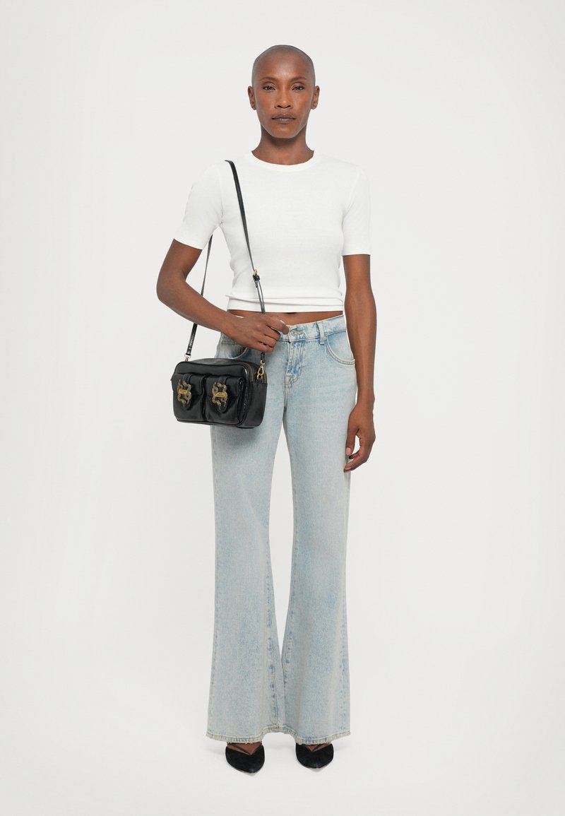 White cropped short-sleeve top, light blue flared jeans, black handbag with gold accents, and black pointed-toe heels.