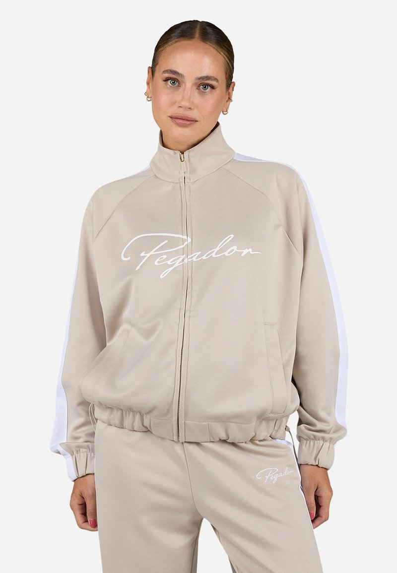 Sweatshirt beige zippé avec des panneaux latéraux blancs et le logo "Pegadon". Il présente un col haut et des poignets froncés, fabriqué à partir d'un tissu lisse et doux.