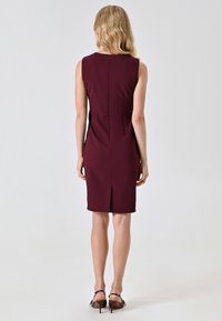 Abito senza maniche di colore bordeaux con uno spacco sul retro, vestibilità sartoriale, tessuto morbido e chiusura con zip sul retro. Texture liscia con dettagli minimi.