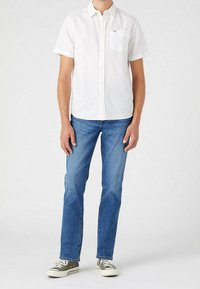 Biała koszula krótki rękaw z guzikami, z kieszonką na piersi, zestawiona z niebieskimi dżinsami i szarymi trampkami. Prosty krój z luźnym krojem.