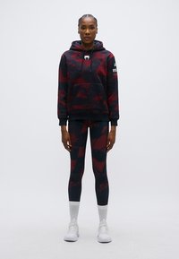 Sweat à capuche camouflage rouge et noir avec cordons et poche avant, assorti à un legging assorti présentant un motif similaire et une coupe ajustée.