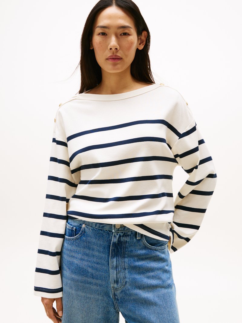 Camisola de manga longa às riscas em creme com riscas azul-marinho, com um decote largo e detalhes de botões nos ombros, combinada com uns jeans azuis.