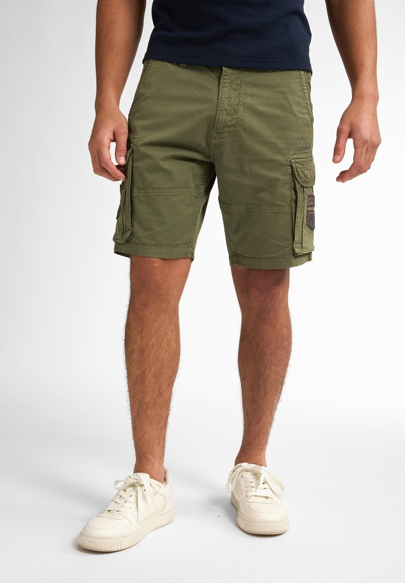 Olive green cargo shorts with multiple pockets, a straight cut, and a durable fabric. Worn with white sneakers.