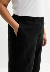 Pantaloni in lino neri con una vestibilità rilassata, dotati di tasche laterali e una cintura elastica. Texture liscia e design minimalista.