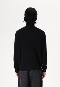 Pull noir à col roulé côtelé avec manches longues, doté d'un col haut et d'une coupe décontractée, présenté de dos.