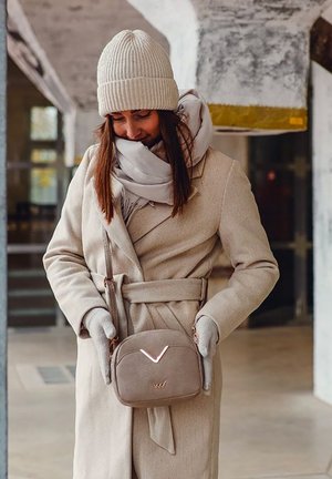 Beige vlněný kabát se zavázaným pasem, doplněný o světlou šedou šálu a žebrovanou krémovou čepici. Malá hnědá crossbody taška s zlatými akcenty.