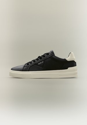 Baskets basses noires avec semelle blanche et patch au talon, lacets noirs, et logo "REPLAY" sur le côté.