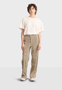T-shirt beige a maniche corte abbinato a pantaloni a vita alta con base beige e stampa animale nera. Tessuto leggero e vestibilità comoda.
