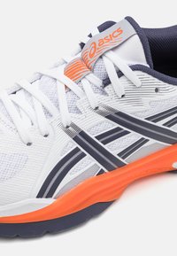 Chaussure de sport blanche avec accents gris et marine, tige texturée, détails orange et rainures multidirectionnelles sur la semelle pour une meilleure traction.