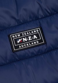 Marineblaues gestepptes Stoff mit einem rechteckigen schwarzen Patch. Der Patch zeigt weißen und roten Text: "NEUSEELAND", "N.Z.A" und "AUCKLAND."
