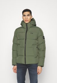 Giacca verde imbottita con chiusura a zip, cappuccio regolabile e dettagli neri. Presenta un design trapuntato e tasche frontali.
