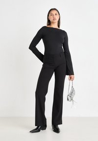 Black long-sleeve top with a square neckline paired with black flared pants. Accessory: small silver handbag with chain strap and tassel.