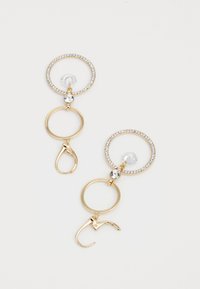 Les boucles d'oreilles en ton doré présentent des designs circulaires ornés de strass transparents et d'un disque suspendu, mettant en avant une finition polie et un style clip-on.