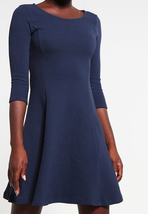 Navyblauwe, geribbelde jurk met een ronde halslijn en driekwartmouwen, die vanaf de taille uitloopt voor een ontspannen pasvorm.