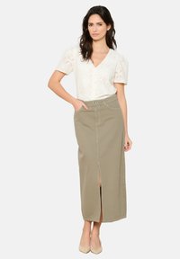 Blouse blanche en dentelle avec des manches courtes bouffantes, associée à une jupe en denim kaki longue avec une fente à l'avant et de subtils détails de couture.