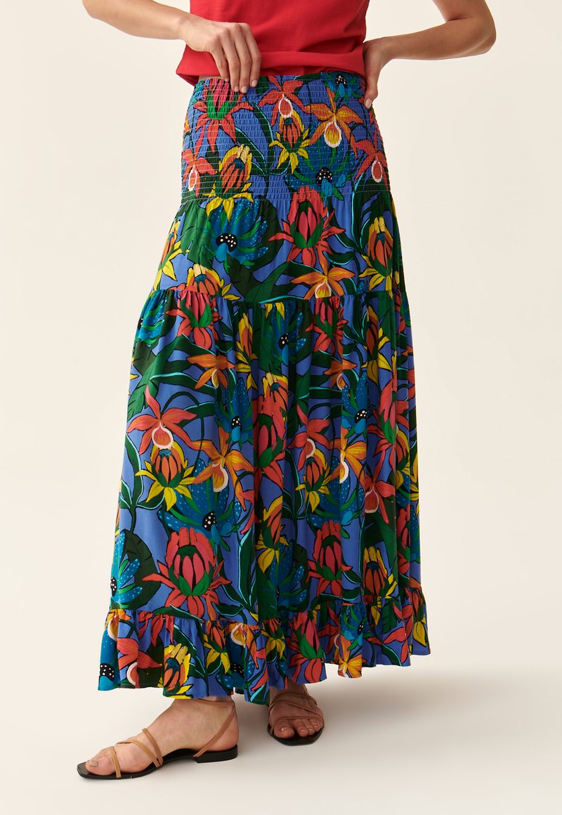 Jupe maxi florale avec taille smockée, présentant des motifs vibrants rouges, jaunes et verts sur un fond bleu ; détail de l'ourlet froncé.