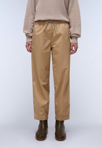 Beige lette bukser med elastisk midjebånd og snøring, med en avslappet passform og oppbrettede hems, iført mørke støvler.