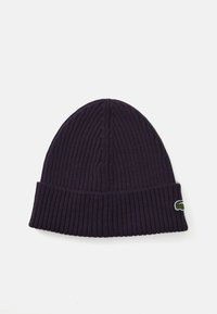 Bonnet en tricot côtelé violet avec un revers plié et un petit logo vert sur le côté. Texture douce, design ajusté.