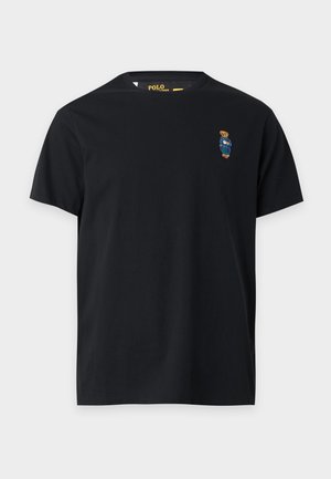 Μαύρο T-shirt με κοντά μανίκια και στρογγυλή λαιμόκοψη με μικρό κεντητό αρκουδάκι που φοράει μπλε σαλόπετα στα αριστερά του στήθους.