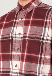 Rød og hvid skotsk ternet flannel skjorte med knaplukning fortil, to brystlommer og en spids krave med en struktureret finish.