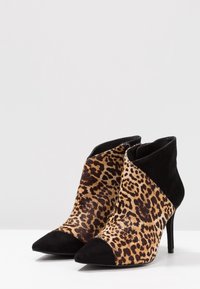 Par de botas de tobillo de tacón alto con estampado de leopardo y acentos de ante negro en la punta y el talón, exhibidas sobre una superficie blanca.